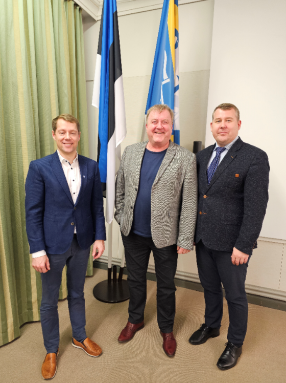 Pildil on kolm meest, Mikk Tuisk, Aivar Mäe ja Koit Voojärv, kes seisavad Eesti lipu ja Saaremaa valla lipu ees.