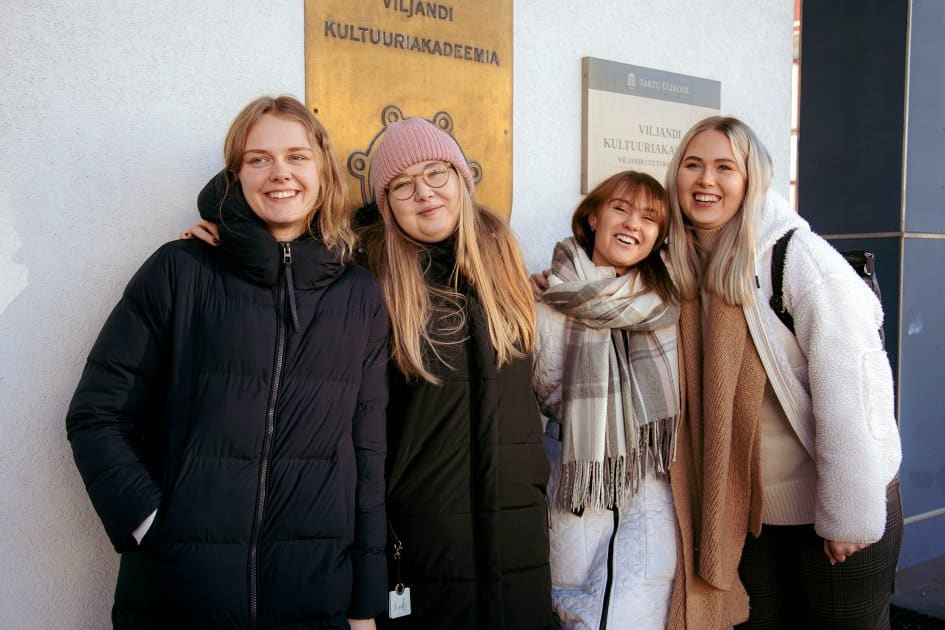 Pildil on neli noort naist, kes seisavad Viljandi kultuuriakadeemia sildi all ja naeratavad.