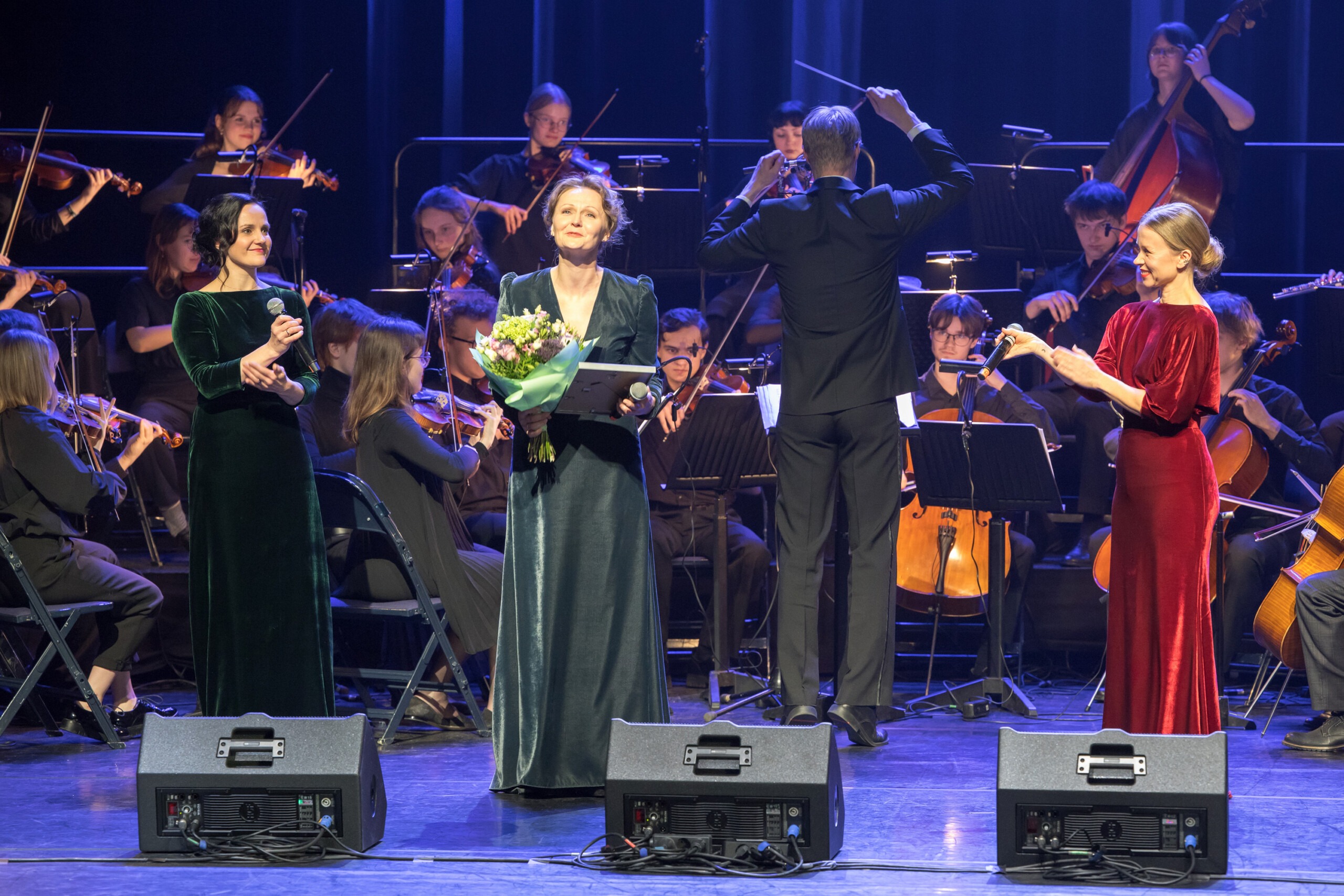 Pildil on Leida Rammo preemia üleandmine Sandra Uusbergile. Uusbergil on käes lillekimp ja diplom, seljas pikk sametine roheline kleit. Tema kõrval aplodeerivad Hele Kõrve ja Evelin Võigemast, taustal mängib orkester.