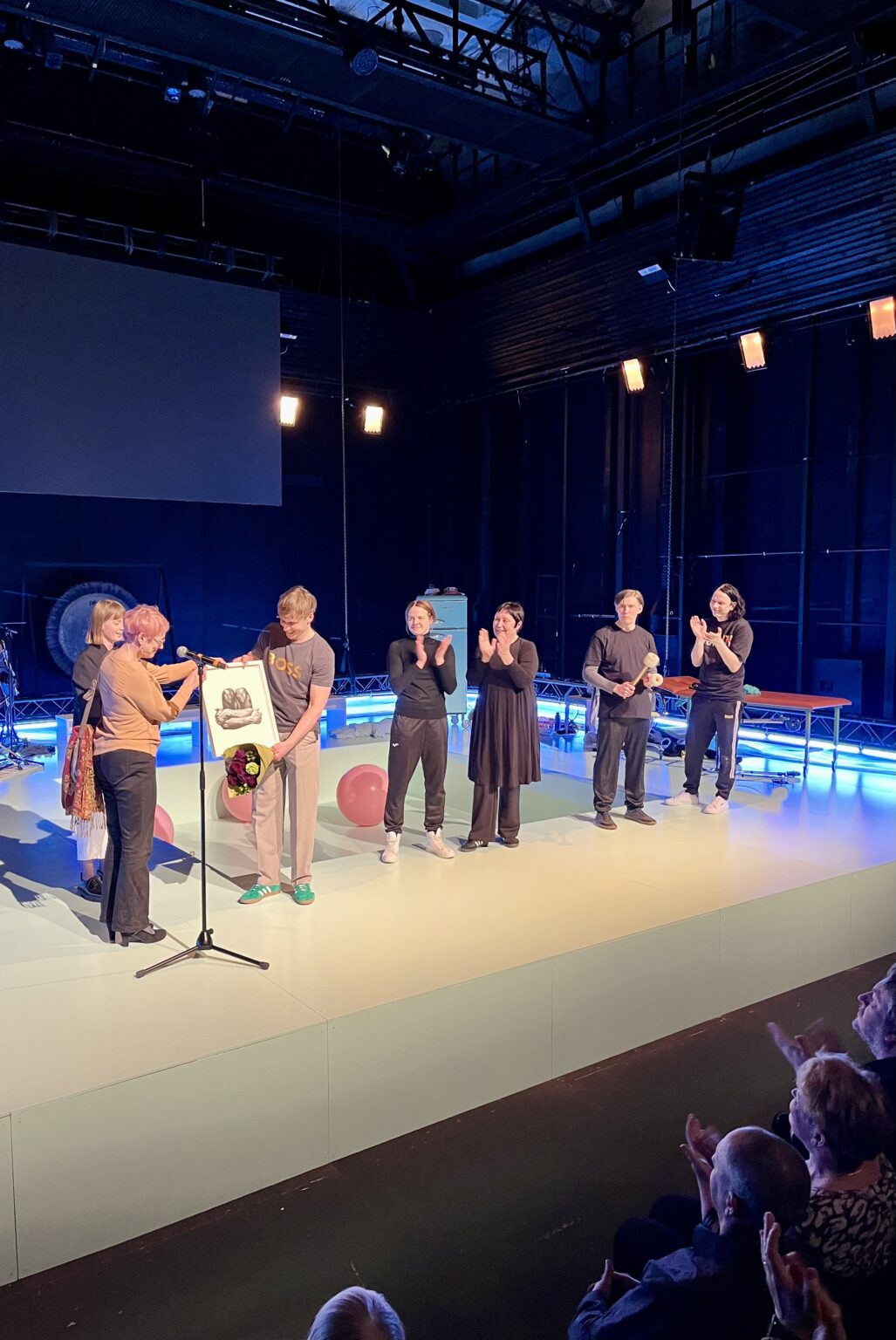 Pildil on Hea Teatri Auhinna üleandmine, mis toimus Sakala 3 teatrimaja laval. Pildil annab Heili Einasto Rasmus Kaljujärvele üle mustvalge kunstiteose, eemal plaksutavad ülejäänud trupiliikmed.