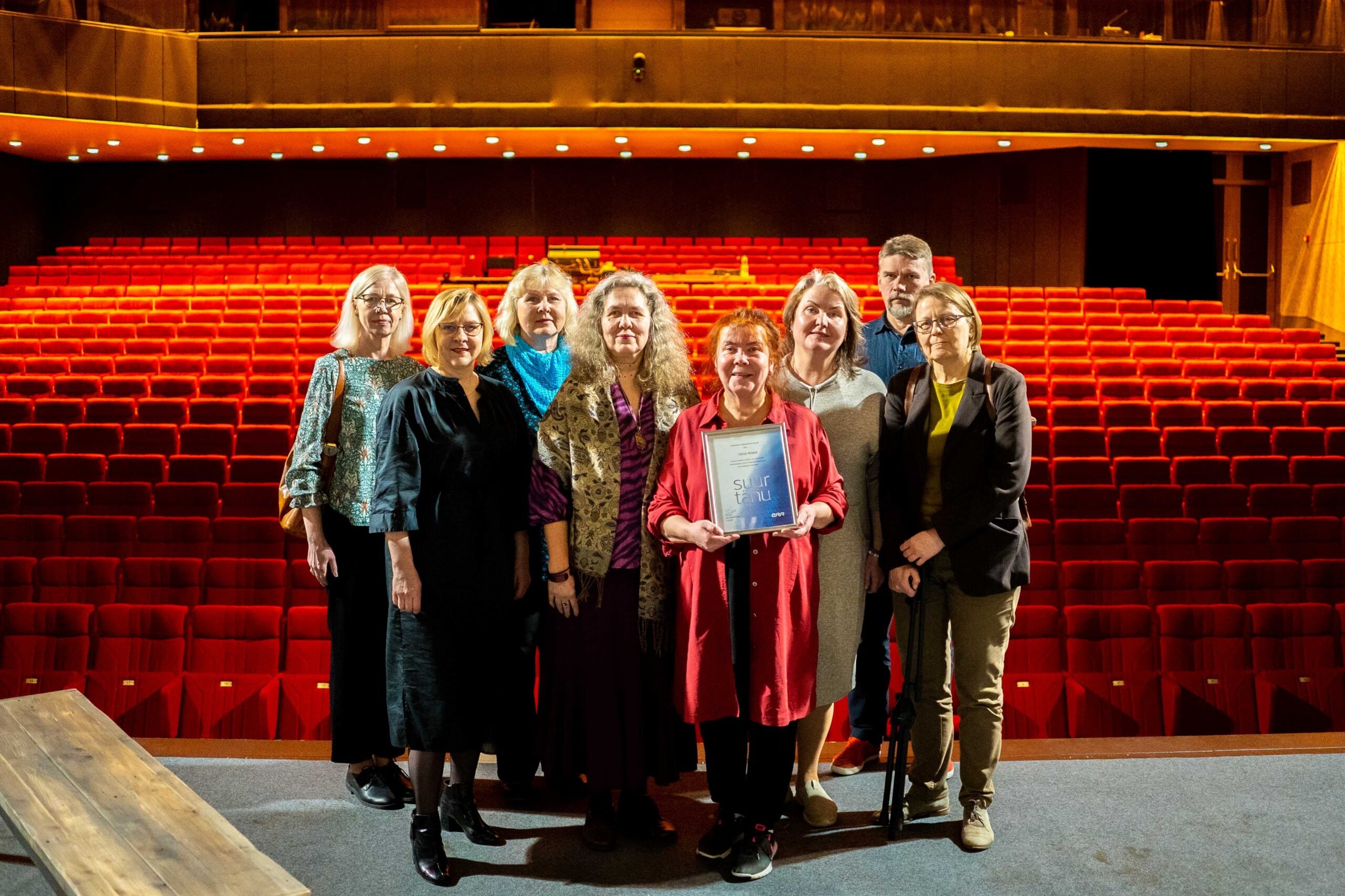 Pildil on neli inimest, kes seisavad Ugala Teatri suure saali laval, selja taga paistmas punased publikutoolid. Esiplaanil on Terje Pennie, kes hoiab käes raamitud diplomit.