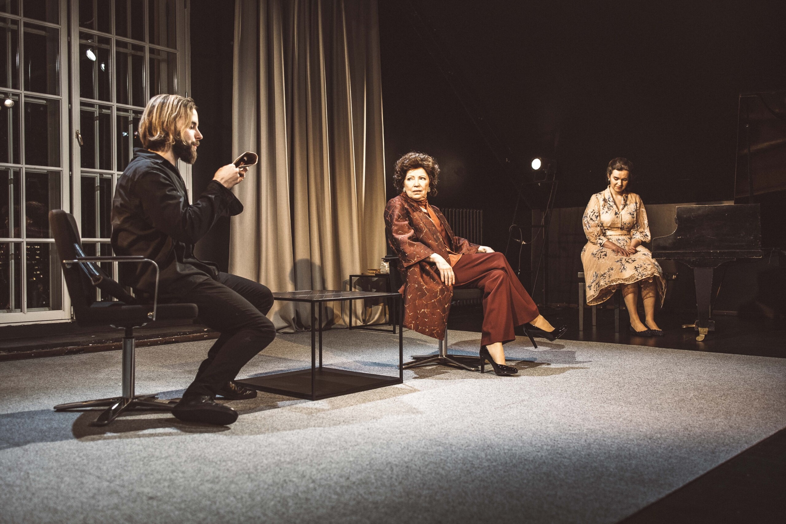 Pildil on stseen lavastusest "Solist". Märten Metsaviir ja Kersti Kreismann istuvad toolidel kahel pool kohvilauda, Metsaviir hoiab käes paberit. Kirke Karja istub eemal klaveri taga.