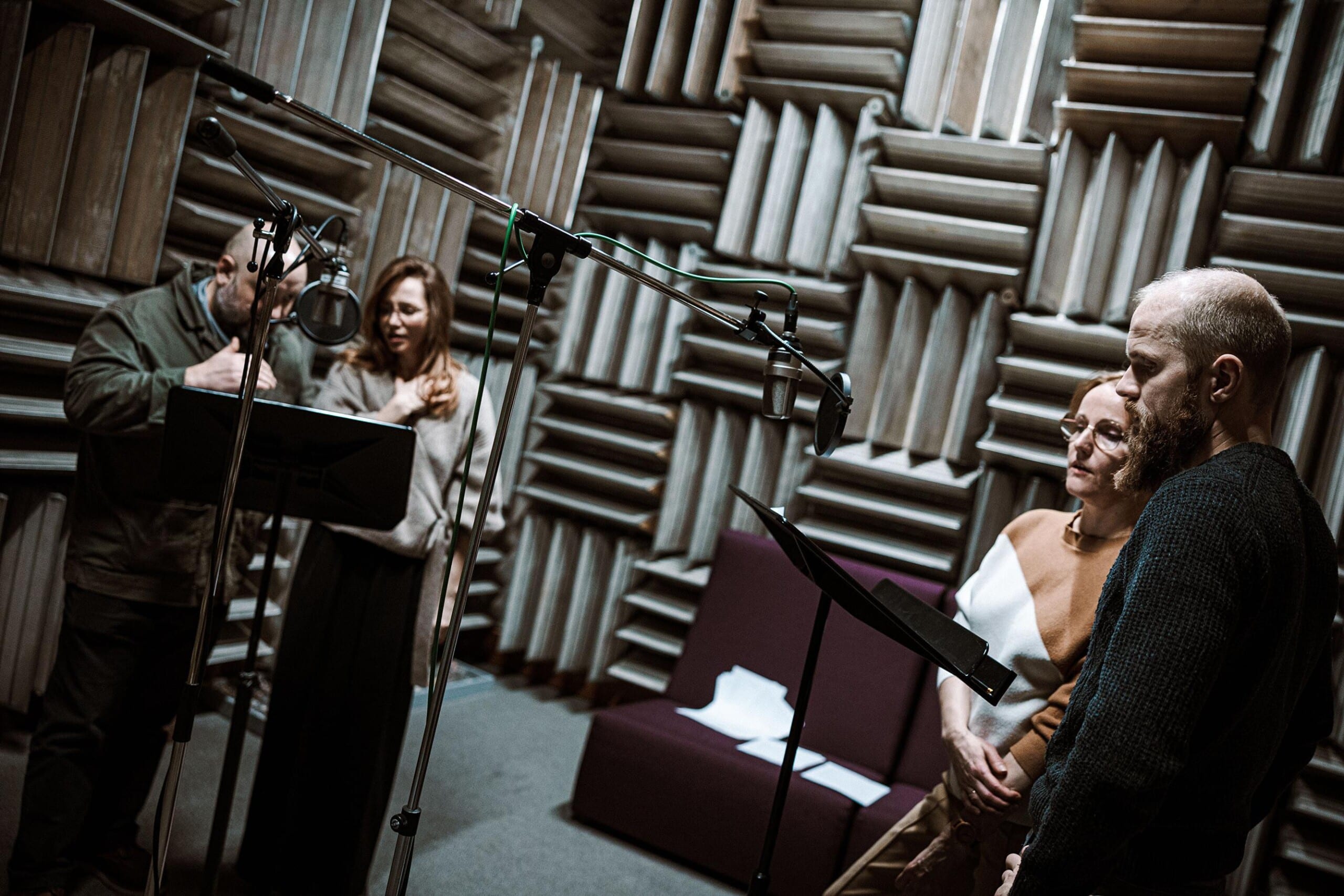 Peeter Rästas, Mirtel Pohla, Liina Vahtrik ja Kristo Viiding seisavad müra summutavate seintega stuudioruumis, nende ees on kaks mikrofoni ja kaks noodipulti.