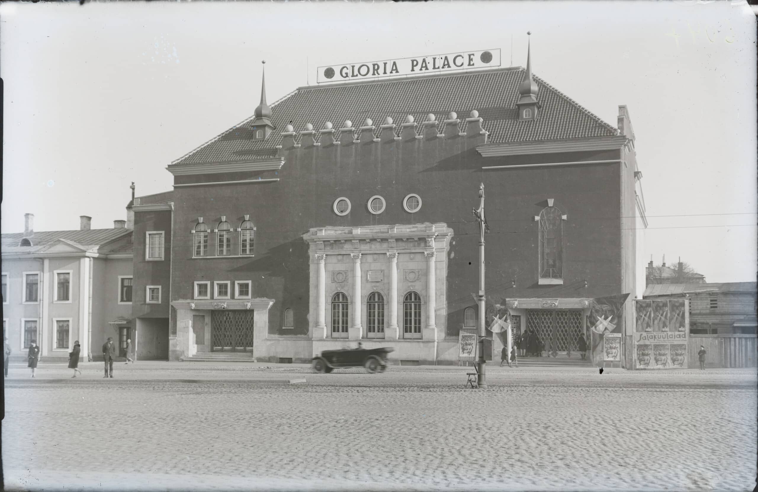 Mustvalgel fotol on kino Gloria Palace: tume mitmekorruseline hoone munakividega platsi ääres. Maja katusel on kaks väikest torni ja silt 