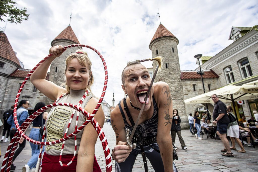 Pildil on kaks tsirkuseartisti Viru väravate ees Tallinnas. Vasakpoolne artist hoiab käes kahte punase-valgekirjut hularõngast, parempoolne väikest mõõka, mis läbistab tema keelt, mis on otsast kaheks jagunenud.