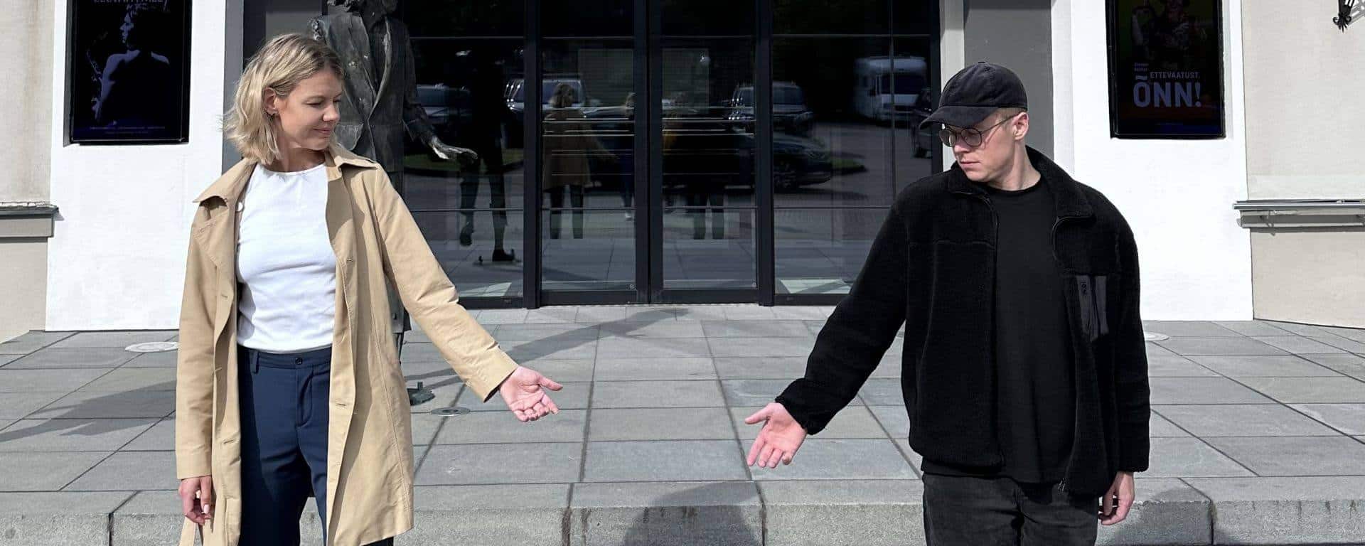 Pildil on näitlejad Laura Niils ja Märten Matsu, kes seisavad Rakvere Teatri suure maja sissepääsu ees. Nende vahel on tühi koht, mille poole nad sirutavad käe ja vaatavad.