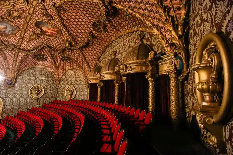 Pildil on Südalinna Teatri suure saali rõdu, kus on näha kuut rida punaseid toole ning kuldsetes toonides mustrilisi lae- ja seinaornamente.