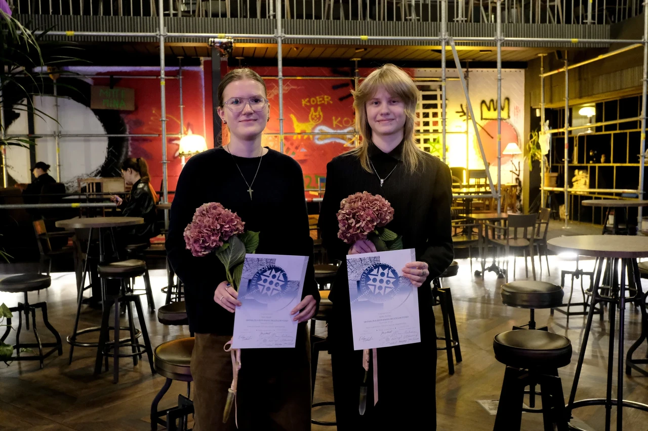 Pildil on kaks noort naist, kes seisavad Von Krahli Teatri kohvikus. Neil on käes ühesugused diplomid ja helelillad lilled.
