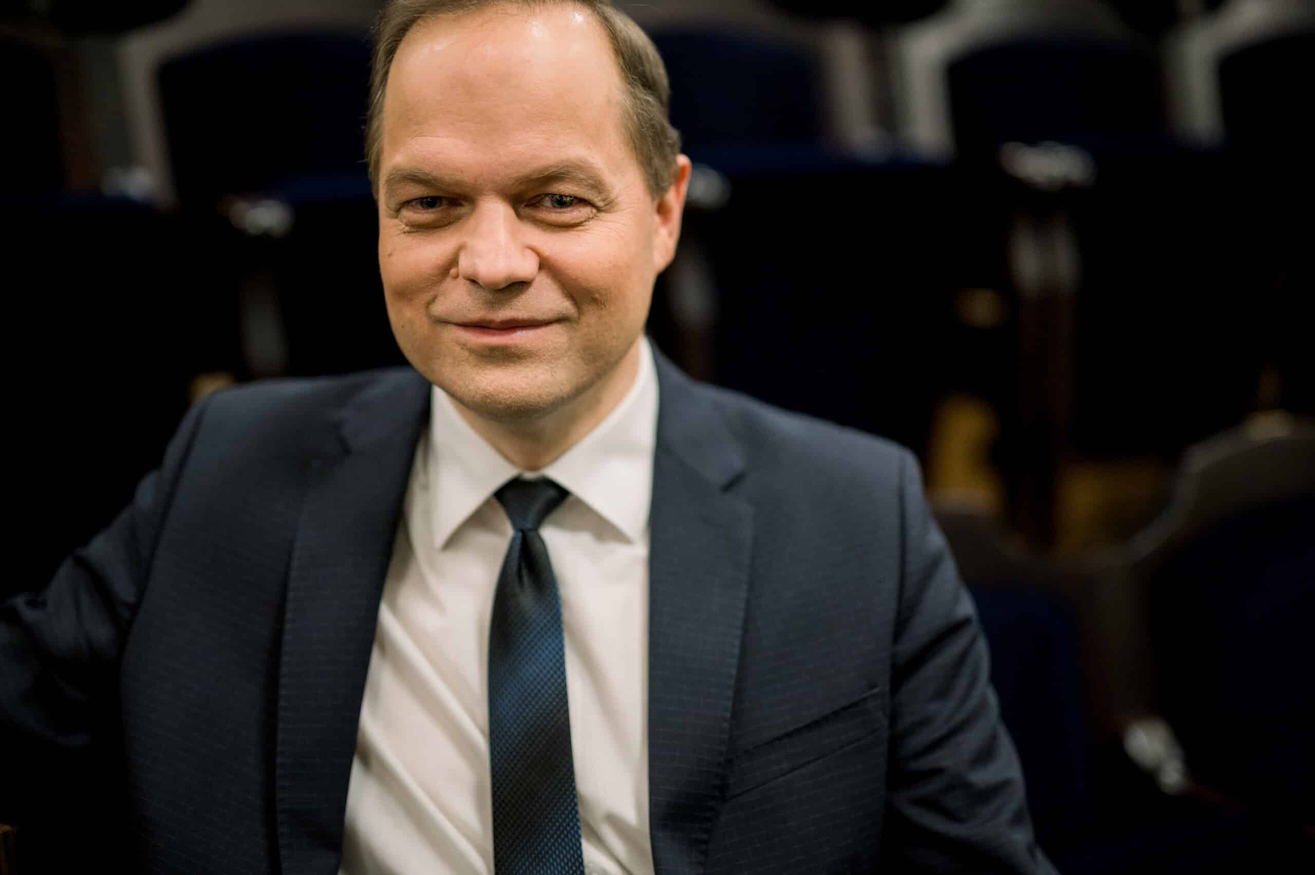 Pildil istub Ott Maaten Estonia teatrisaalis toolil. Tal on lühikesed pruunid juuksed, seljas tumesinine pintsak ja lips ning valge triiksärk.