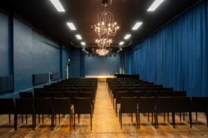 Pildil on Teatri- ja Muusikamuuseumi Peeter Süda nimeline saal. Saalis on tumesinised seinad ja kardinad, mustad toolid, helepruun parkett ning laest ripub kolm lühtrit.