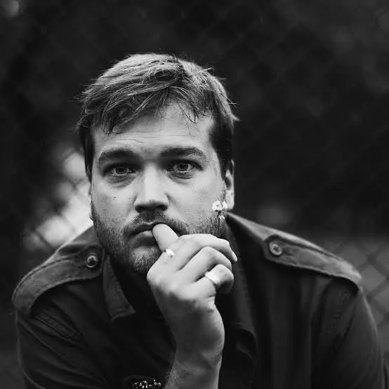 Mustvalgel portreefotol on Johan Elm. Tal on lühikesed juuksed ja lühike habe, ta toetab lõuga oma paremale käele.