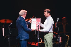 Pildil on Guido Kangur ja Reimo Sagor, kes seisavad laval mikrofonide taga ning Sagor annab Kangurile üle raamitud diplomi. Diplomi keskel on suurelt kirjas 