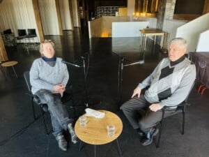 Pildil istuvad Mats Õun ja Priit Vaher toolidel, nende keskel väike puitlaud kahe veeklaasi ja salvrätikutega. Mõlema mehe ees on statiiviga mikrofon.