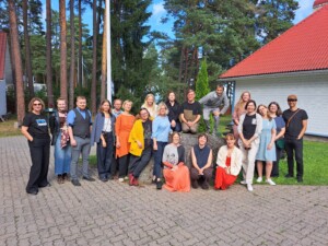 Pildil on 20 inimest, kes seisavad ja istuvad õues sillutatud platsil rändrahnu ümber.