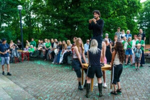 Pildil on Baltoscandali festivali avamine, kus üks etendaja seisab laual ja mängib flööti. Neli etendajat tõstavad lauda samal ajal õhku. Etendajate taga paistab paarikümneliikmeline publik.