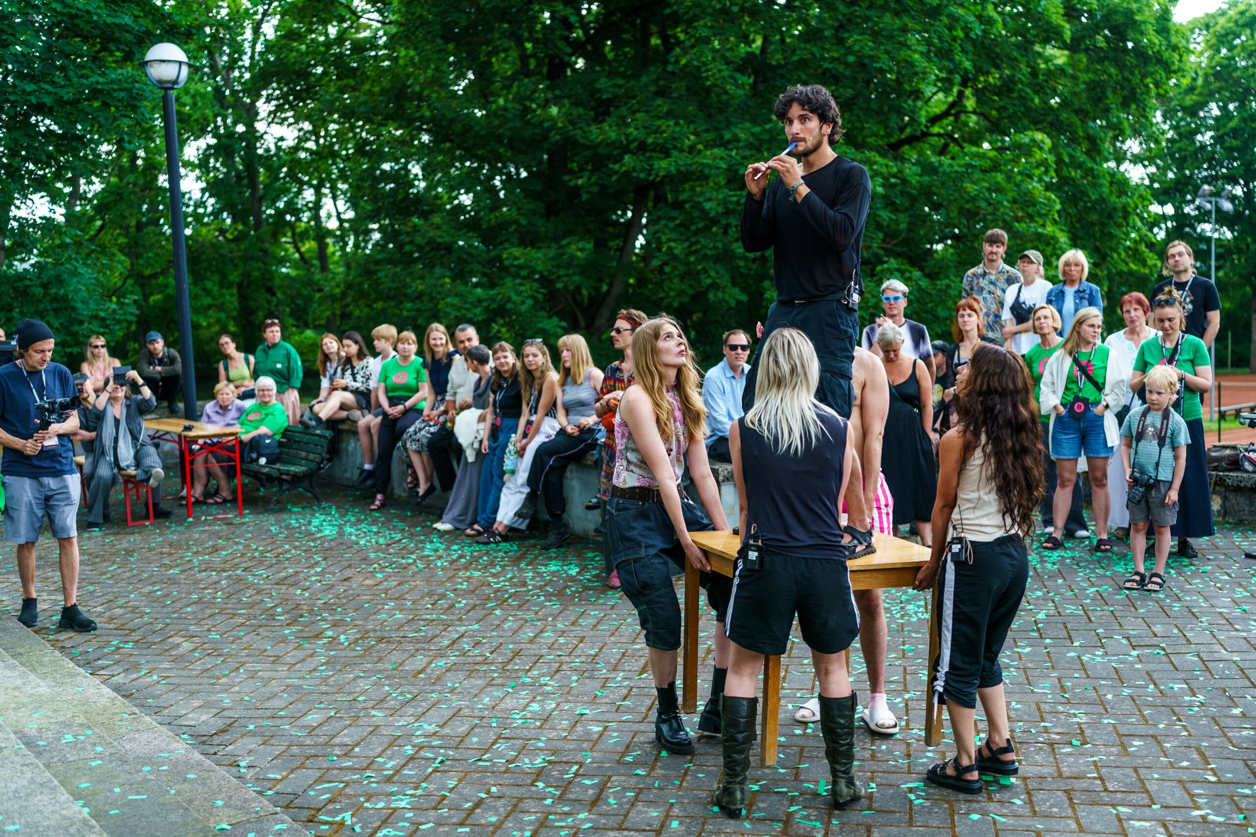 Pildil on Baltoscandali festivali avamine, kus üks etendaja seisab laual ja mängib flööti. Neli etendajat tõstavad lauda samal ajal õhku. Etendajate taga paistab paarikümneliikmeline publik.
