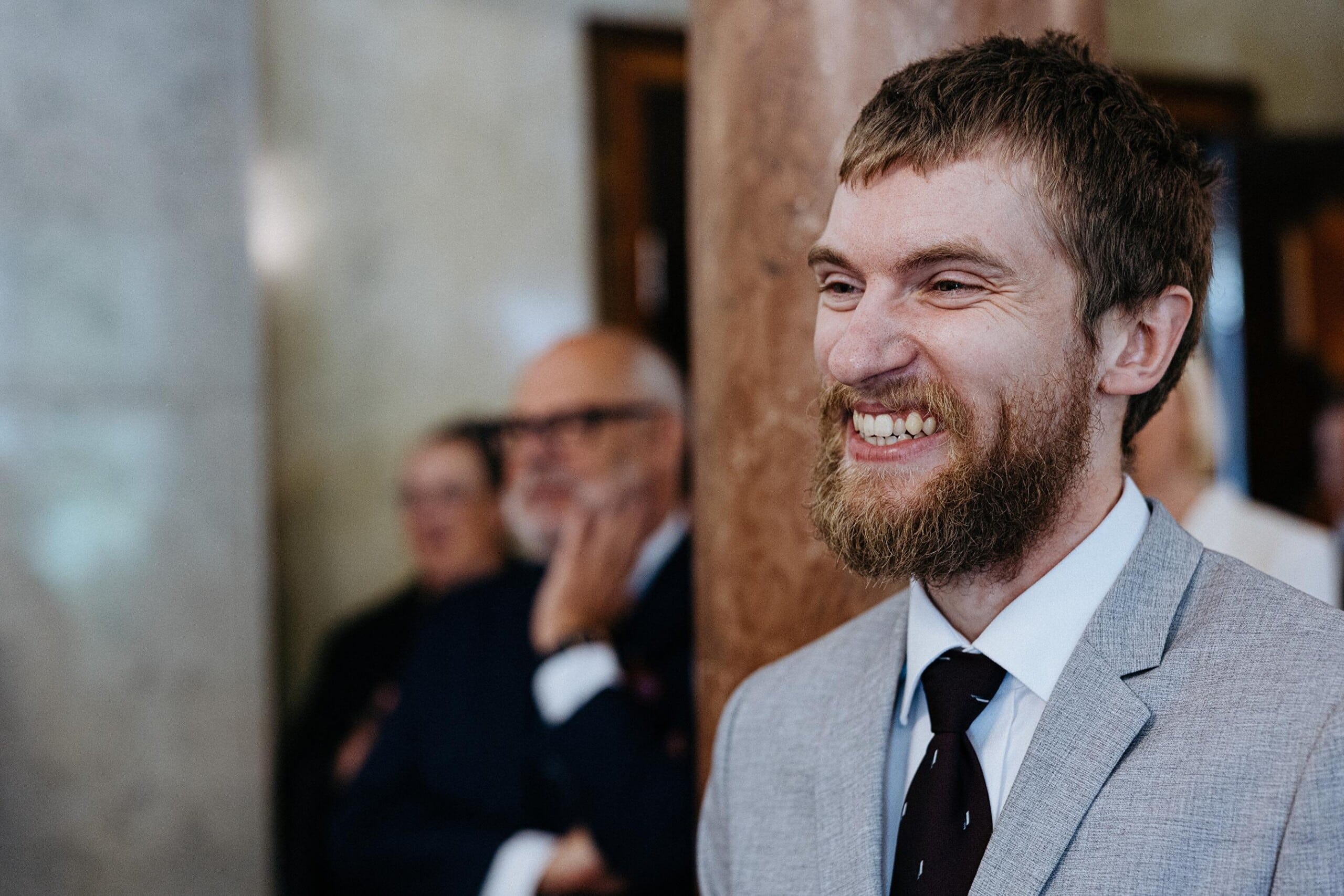 Pildil on Priit Põldma, tal on lühikesed pruunid juuksed ja pruun habe. Tal on seljas hall ülikond ja ta naeratab laialt.