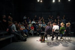 Pildil on Genialistide klubi saal, mille laval istub neli inimest toolidel. Nende vestlust kuulab publikutribüünil mitukümmend inimest.