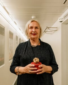 Teatriinfo Pildil on Luule Komissarov, kes hoiab käes Ugala publikupreemiat Kuldõuna. Tegu on väikese skulptuuriga, millel on punane alus ja peal kuldne õun.