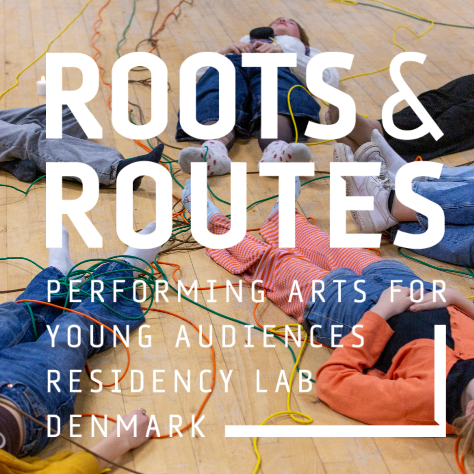 Pildil on noored, kes lamavad ringis põrandal, jalad ringi keskele suunatud. Pildile on valges kirjas kirjutatud "ROOTS & ROUTES / PERFORMING ARTS FOR YOUNG AUDIENCES RESIDENCY LAB DENMARK".